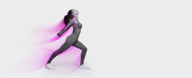 Spor kıyafetli genç Afro-Amerikalı kadın hamlede arka büküm performansı sergiliyor, sırt kaslarını esnetiyor, pembe stüdyo arkaplanı üzerinde. Spor salonu rutini ve spor salonu. Tam uzunluk