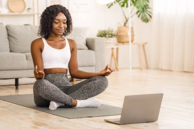 Huzurlu siyah kadın evde dizüstü bilgisayarın önünde meditasyon yapıyor, yoga online konsepti, boş alan