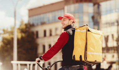 Yemek Teslimatı. Sarı sırt çantalı profesyonel kurye Bisikletle şehre yiyecek getiriyor. Boş Boşluk