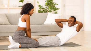 Genç siyah çift evde birlikte egzersiz yapıyor, karın kasları üzerinde çalışıyor.