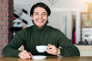 Kafede tek başına çay ya da kahve içen neşeli genç adam.