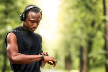 Modern teknolojiler ve aktif yaşam tarzı. Siyah atletik adam spor bilekliğiyle çalışıyor, bulanık park geçmişi var.