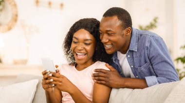 Neşeli Afrikalı çift akıllı telefondan oyun oynuyor, ev içi, kopyalama alanı