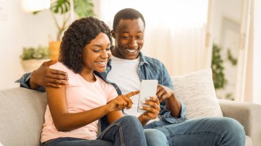 Heyecanlı siyah çift yeni mobil uygulamayı kontrol ediyor, ev içi, kopyalama alanı