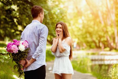 Sevecen erkek arkadaşı parkta sevgili kız arkadaşı için bir buket çiçek saklıyor, boşluğu kopyalıyor.