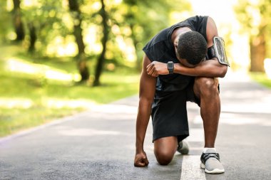 Üzgün Afro-Amerikan sporcusu park yolunda duruyor, kaybolmuş hissediyor.