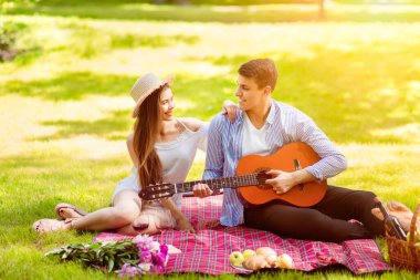 Yakışıklı genç adam parkta yaz pikniğinde sevgilisine romantik bir şarkı söylüyor.