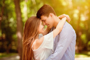 Milenyum çifti parkta romantik bir buluşmada kucaklaşıp alnına dokunuyor.