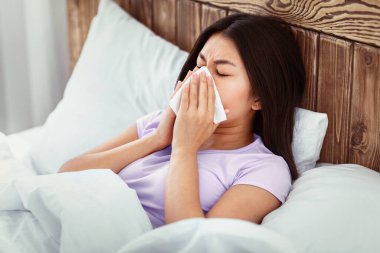 Rhinitis. Hasta Çinli Kadın kağıt mendilde burnunu siliyor. Evde yatağında grip oluyor..