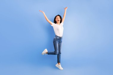 Zaferin sevinci. Mavi stüdyo duvarının üzerinden atlayan ve el kaldıran neşeli kadın. Tam uzunluk, boş boşluk
