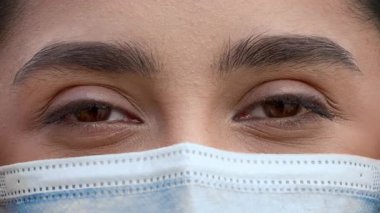 Kahverengi saçlı genç bir Arap kadın açık havada güneşli bir günün tadını çıkarıyor. Bir maske takıyor, şehir hayatı ile uğraşırken etkileyici kahverengi gözlerini ve doğal güzelliğini ön plana çıkarıyor..