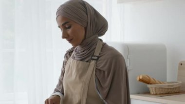 Modern bir mutfakta, önlüklü bir Orta Doğulu kadın taze sebzeleri yemek için doğrar..