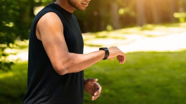 Tanımlanamayan siyahi sporcu parkta koşarken kamerasını kontrol ediyor, boş bir alanda. Panorama