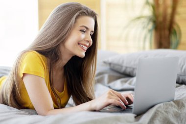 Laptopuyla yatağında yatıp internette gezinen çekici milenyum kadını.