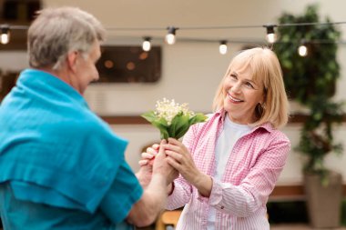 Kıdemli adam, karavanının yanındaki karısına çiçek veriyor.