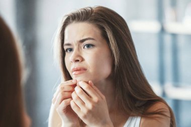 Deri sorunu. Genç kız banyoda aynanın önünde sivilcesini sıkıyor.