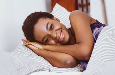Gülümseyerek sabah. Çekici Afrikalı Amerikalı genç bayan yatak odasında iç tarafta yatıyor.