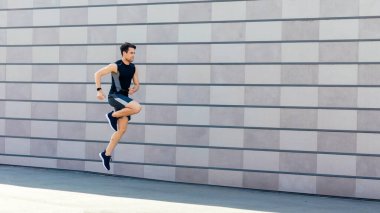 Eğitimde havada donmak. Gri duvar arka planında, sokakta atlayan ve koşan zayıf adam, boş alan