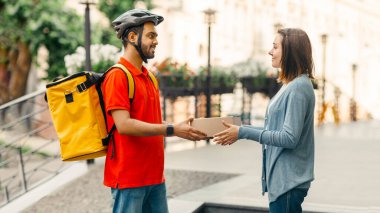 Kadın kuryeden online alışveriş yapıyor. Kasklı teslimatçı, sarı sırt çantalı müşteriye sokakta, evin yanında bir kutu verdi.