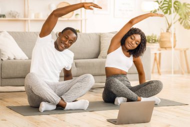 Spor yapan Afrikalı çift evde birlikte esniyor, dizüstü bilgisayardan ders izliyorlar.