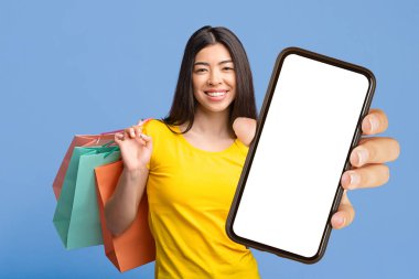 İnternetten alışveriş uygulaması. Gülümseyen Asyalı Kadın elinde akıllı telefon, siyah perde ve alışveriş torbaları, mor arka planda poz veren,