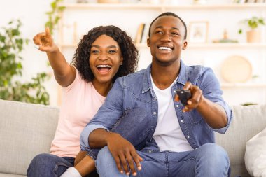 Duygusal Afrikalı erkek ve kadın evde televizyon izliyor, kadın işaret ediyor ve gülüyor, boşluğu kopyalıyor.