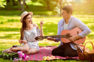 Romantik erkek arkadaş parkta yaz pikniğinde kız arkadaşına gitar çalıp şarkı söylüyor.