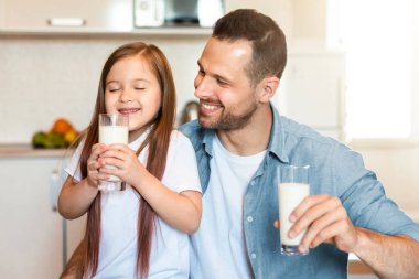 Mutlu baba ve kız süt içerek evde mutfaktaki masada oturarak kahvaltı yapıyorlar. Aile Beslenme ve Süt Ürünleri