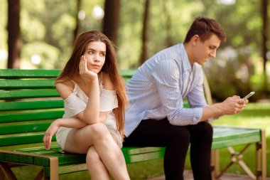 Gadget bağımlılığı konsepti. Sıkıcı genç kız ve erkek arkadaşı parkta sıkıcı bir randevuda cep telefonunda sıkışıp kalmış.