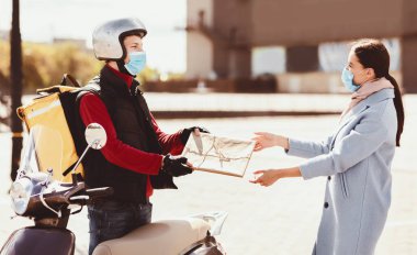 Güvenli Nakliye Servisi. Korumalı Maskeli Kurye Şehir Bölgesi 'nde Scooter' la bekleyen müşteriye paket getiriyor..