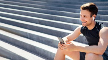 Sosyal ağ, blog ve spor. Kablosuz kulaklıklı, gülümseyen bir sporcu akıllı telefona bakar ve merdivenlere oturur.
