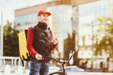 Yemek teslimatı. Kurye Adam Smartphone 'u tutuyor Öğle yemeklerini getiriyor Bisikletle şehrin yakınındaki İş Merkezi' ne gidiyor. Boşluğu Kopyala
