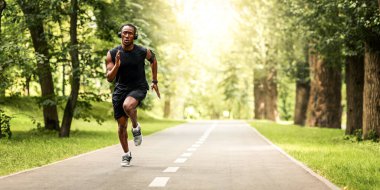 Konsantre siyahi adam yazın park yolunda koşuyor, boşluk var.