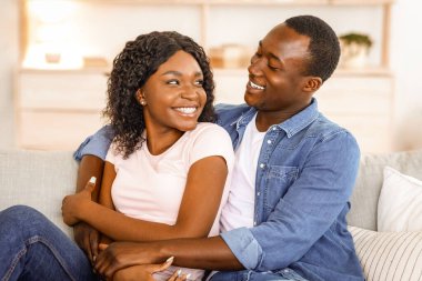 Afrikalı evli çiftler evlerinde vakit geçirir, kanepede dinlenirken kucaklaşır ve sohbet ederler.