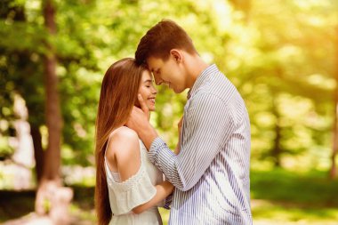 Romantik bir ilişki. Yakışıklı genç adam ve kız arkadaşı yaz günü parkta sarılıyorlar.