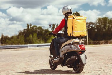 Yemek Teslimat Servisi. Sarı Sırt çantalı Kurye Scooter 'a biniyor ve şehir dışındaki restoranları dağıtıyor. Geri Görünüm, Boş Boşluk