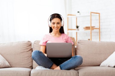 İçişleri Bakanlığı. Dizüstü bilgisayarda çalışan, kanepede oturup kulaklıkla müzik dinleyen mutlu bir kız.