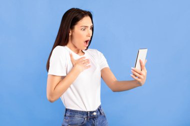 Şok edici haberler. Akıllı telefon tutan kız internet haberlerini okuyor. Mavi stüdyo duvarının yanında duruyor. Kopya alanı.