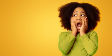 Omg. Şok olmuş küçük bir kızın portresi şaşkınlıkla yüzüne dokunuyor ve sarı arkaplandaki fotokopi alanına bakıyor.,