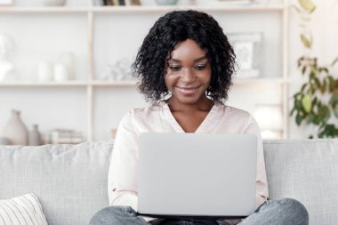 Serbest Kavram. Siyah Milenyum Kadını dizüstü bilgisayarda çalışıyor evdeki koltukta oturuyor, şık oturma odasında oturuyor, boş yer var.