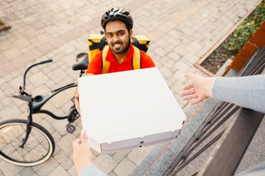 İnternetten sipariş ve evde pizza. Kasklı gülümseyen kurye müşteriye kutularını veriyor, caddenin yanında, manzaralı, pov