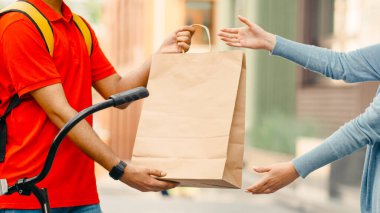 Bisikletli kuryeyle online alışveriş ve teslimat. Sırt çantası ve akıllı saati olan bir adam müşteriye kese kağıdı verir, dış görünüş, boş alan