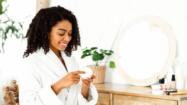 Günlük Skincare. Güzel siyah kadın evde cildine nemlendirici krem sürüyor, kendini güzellikle şımartıyor, boşluğu kopyalıyor.