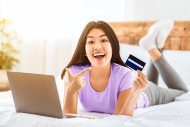 Çevrimiçi satış. Koreli kadın evde yatağında dizüstü bilgisayar ve kredi kartı kullanarak alışveriş yapıyor. Mutlu Alıcı.