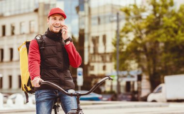 Kurye Servisi. Telefonla konuşan teslimatçı bisikletli adam şehre yiyecek teslimatı yapıyor. Metin için Boş Alan