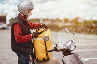 Kurye Servisi. Teslimatçı Çocuk, içinde yiyecek paketleri olan sarı çantayı açıyor Motosikletin yanında duruyor, Cafe Menüleri dışarıda bekliyor..