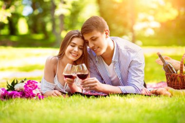 Şefkatli genç bir çift piknik battaniyesinde uzanmış kırmızı şarap bardaklarıyla, açık havada