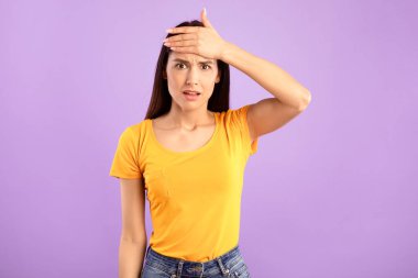 Hasta, korkmuş genç bir kadın, alnına dokunuyor, ateşi ya da baş ağrısı var, stüdyo ortamındaki mor arka planda izole edilmiş,