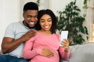 Mutlu siyahi çift evde dinlenirken, akıllı telefon kullanarak selfie çekiyor.