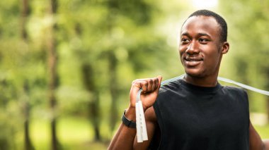 Spor aletleri ve ekipman konsepti. Parkta ip atlama eğitimi almış, boş alana bakan gülümseyen Afrikalı adam.